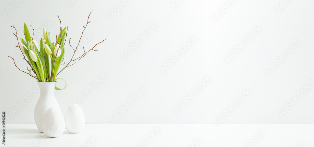 White spring tulips in a vase, easter eggs on a white table. Mock up for displaying works White spring tulips in a vase, easter eggs on a white table. Mock up for displaying works
