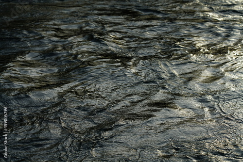 Schnell fließender Fluss mit sich spiegelndem, gold schimmerndem Sonnenlicht