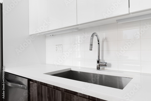 A detail shot of a kitchen sink with white and wood modern cabinets, chrome faucet, and subway tile backsplash.