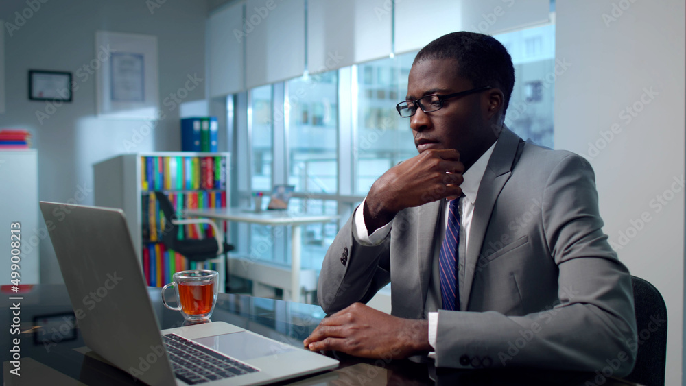 Portrait of pensive African-American investor look at laptop screen in modern workplace