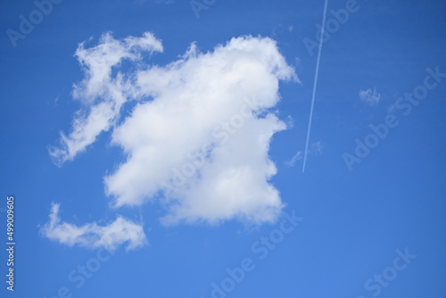 Airplane flying leaving chemtrails next to a big white cloud. Blue clear sky.