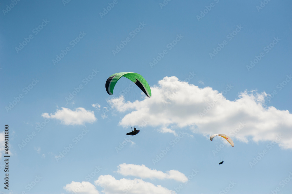 Two paragliders flying in the blue sky against the background of clouds. Paragliding in the sky on a sunny day. Two paragliders flying in the blue sky against the background of clouds. Paragliding in the sky on a sunny day.
