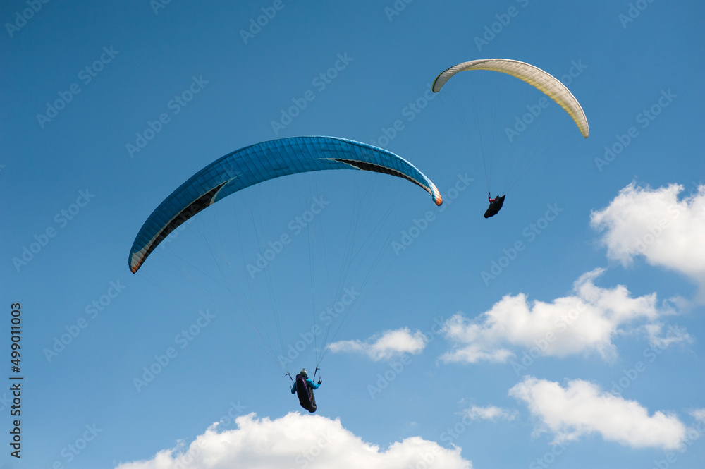 Two paragliders flying in the blue sky against the background of clouds. Paragliding in the sky on a sunny day. Two paragliders flying in the blue sky against the background of clouds. Paragliding in the sky on a sunny day.