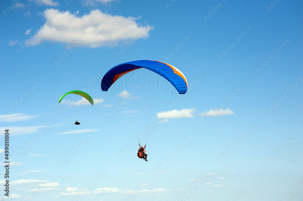 Two paragliders flying in the blue sky against the background of clouds. Paragliding in the sky on a sunny day. Two paragliders flying in the blue sky against the background of clouds. Paragliding in the sky on a sunny day.
