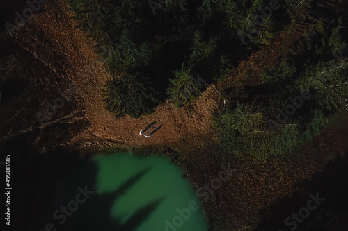 Aerial view of two people standing by the natural lake surrounded by pine trees in Karpaty Mountains  Ukraine.