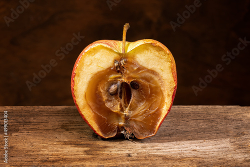 A rotten moldy apple, decomposing, on an wooden shelf. Close-up.