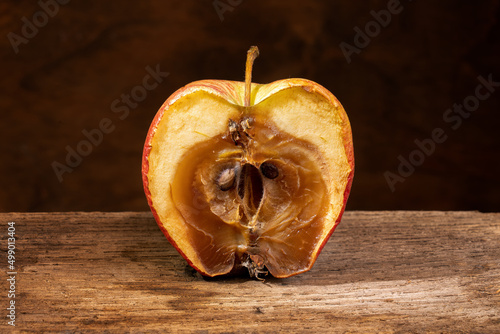 Фотография A rotten moldy apple, decomposing, on an wooden shelf. Close-up.