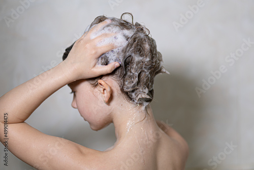 Little, beautiful girl, baby bathes sitting in a white bath with soap suds, shampoo and washes her head with hair. Model photography.