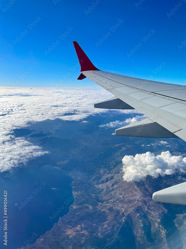 Obraz premium View from the porthole on the wing of an airplane flying above the clouds, mountains are visible below.