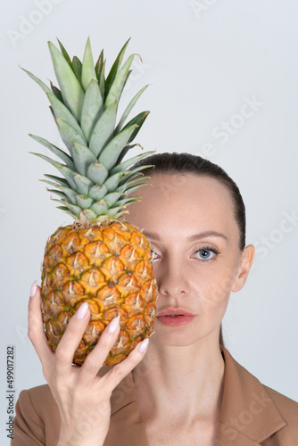 Woman in a business beige jacket. He holds a ripe juicy pineapple in his hand. The concept of healthy and diet food.