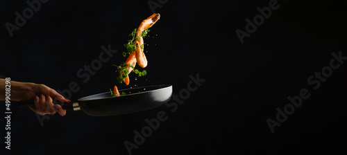 Shrimps with parsley in a pan in a frozen flight. Isolated on black background. Sea cuisine, seafood recipes, restaurant and home cooking. There are no people in the photo.