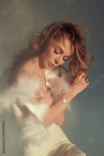 Young attractive women model presenting your jewelry .Wearind white dress with feathers. Nude makeup, perfect skin, long hair. White background.