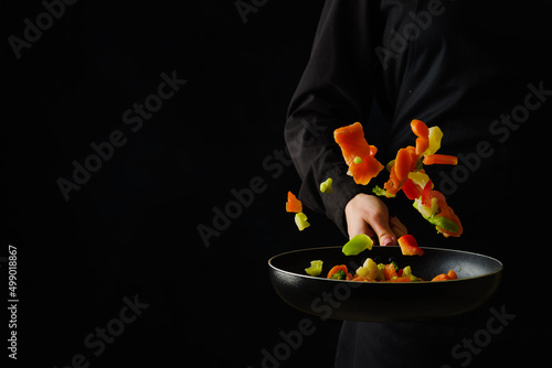 Pieces of red fish - salmon, trout with vegetables in a pan in a frozen flight in the hands of a professional chef. Isolated on black background. Recipes for restaurant and home cooking.