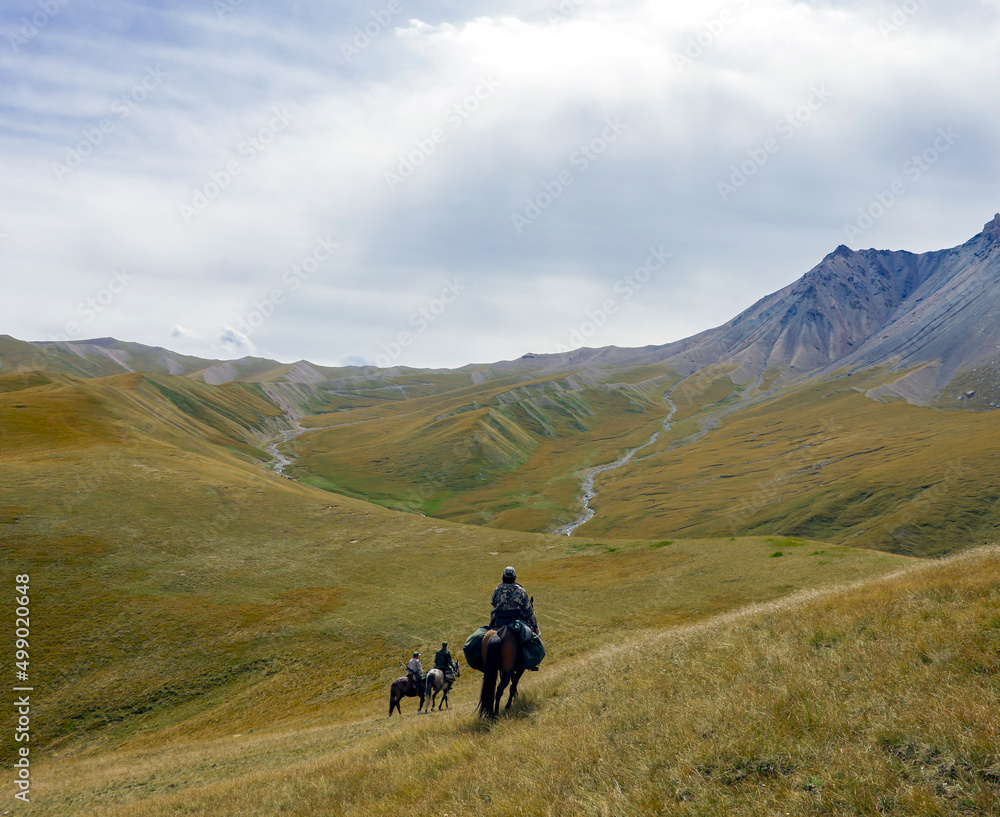 Riders with weapons on three horses move in mountainous terrain.