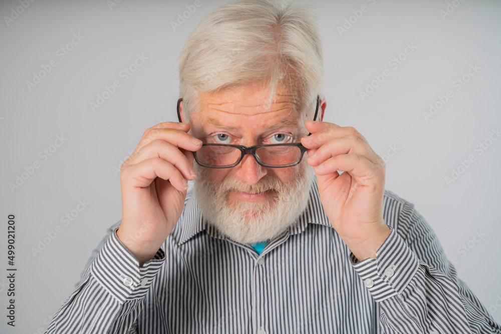 portrait  elder senior man holding eyeglasses, with a beard and gray hair looks from under forehead and holds glasses with his hands.