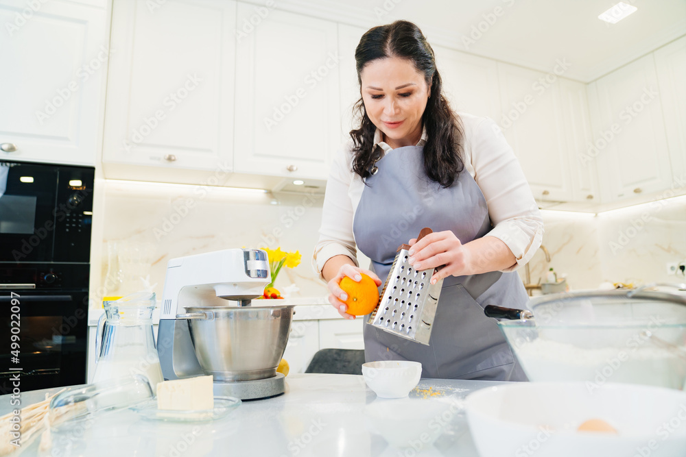a woman cook makes orange zest on a grater to make pastries or cream. a woman cook makes orange zest on a grater to make pastries or cream.