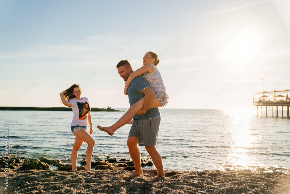 Dad rides his daughter on back on the seashore. 