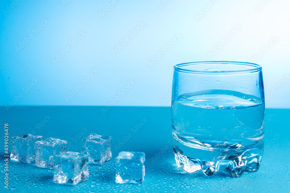 Glass with water and ice cubes nearby Glass with water and ice cubes nearby