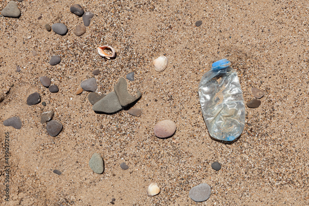 Plastic garbage on the beach. Single-use plastic bottle thrown by sea wave on shore. Concept - Pollution of world ocean by household waste Plastic garbage on the beach. Single-use plastic bottle thrown by sea wave on shore. Concept - Pollution of world ocean by household waste