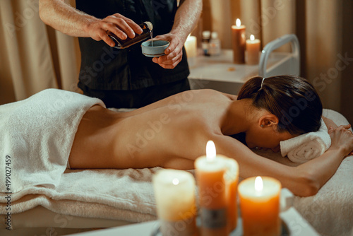 Masseur man therapist preparing warm infused oil to make spine massage