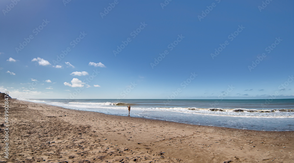 unrecognizable older woman standing alone in the immensity of the beach contemplating the sea
