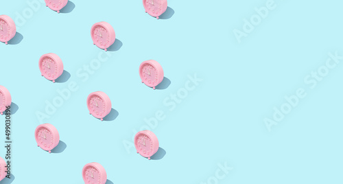Trendy pattern made with pink clock on bright and pastel blue background. Minimal time concept. Chrismas eve or new year idea.