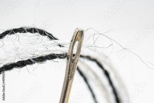 The hole of a metal needle for thread. Macro photo. Sewing needle and black, white threads and microfibres. photo