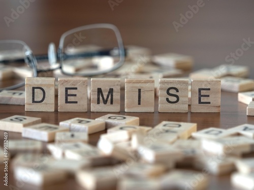 demise word or concept represented by wooden letter tiles on a wooden table with glasses and a book