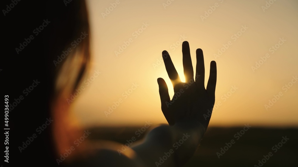 Childhood dream, reach for sun. Girl child with long hair plays with her hand in sun. Hand of tender girl at dawn. Sun between fingers of child, girl. Happy family, travel. Prayer to sun. Child, game