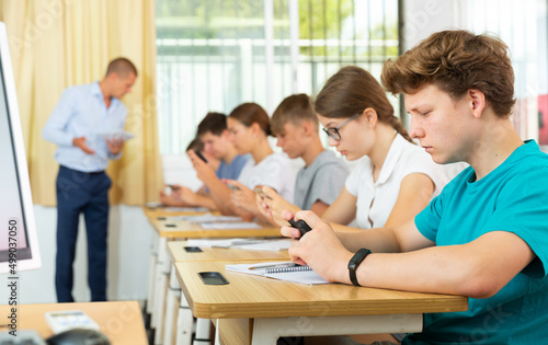 Pupils sitting in class room and watching in their smartphones.