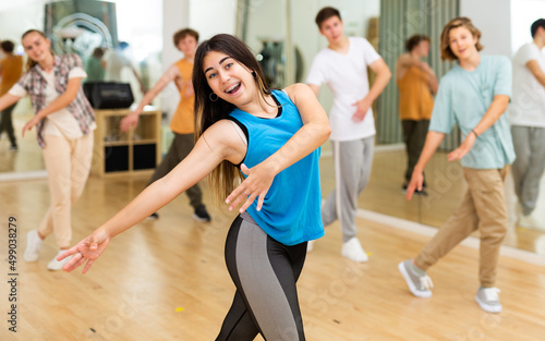 Cheerful emotional teen girl enjoying while training movements of modern group dance in choreography class .