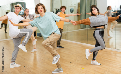 Interested modern teen boys and girls practicing dynamic boogie-woogie in pairs during group class in dance studio for youth