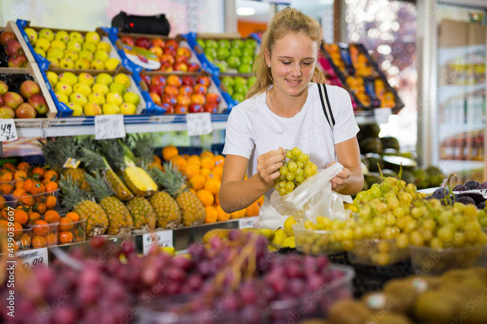 Portrait of beautiful russian young woman buying fresh grape at grocery shop