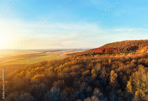 Aerial view of hills covered with dark mixed pine and lush forest with green and yellow trees canopies in autumn mountain woods at sunset. Beautiful autumnal evening landscape © bilanol