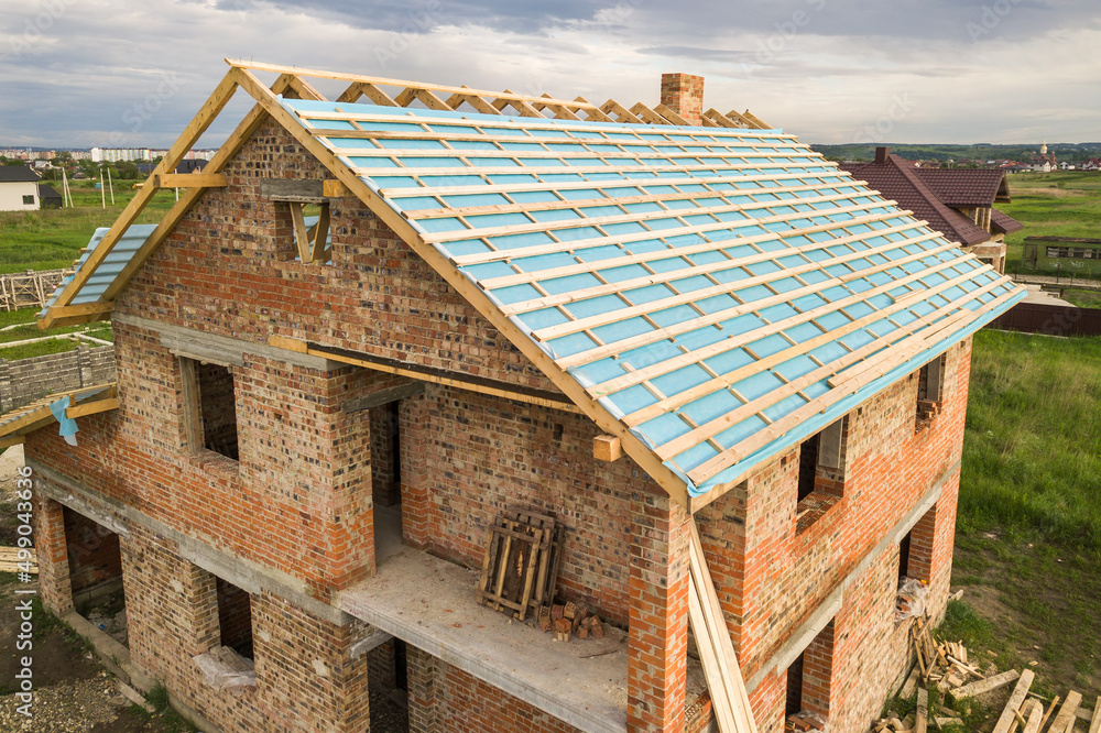 Aerial view of a brick house with wooden roof frame under construction. Aerial view of a brick house with wooden roof frame under construction.