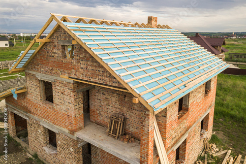 Aerial view of a brick house with wooden roof frame under construction.