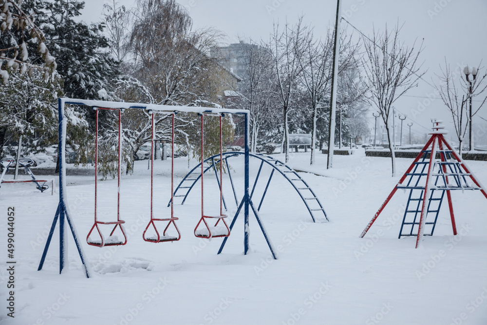 Φωτογραφία Old children playground, slides and swings, in a park covered in snow in Serbia, in Eastern Europe, during a freezing dark evening winter afternoon with residential buildings in background