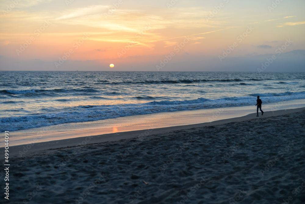 Santa Monica, California, USA - April 10, 2022: A man is walking along Santa Monica Beach during the sunset