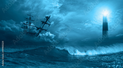 An old sailing ship in the mist sails towards the rocks with amazing lighthouse - Sailing old ship in a storm sea in the background stormy clouds