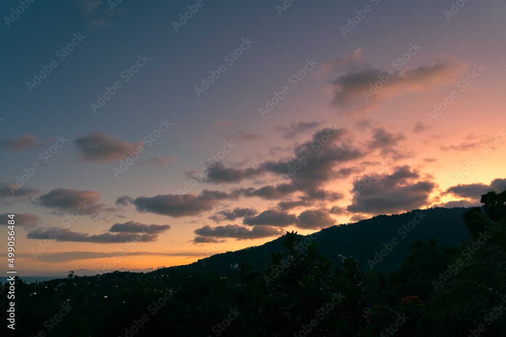 Colorful cloudy sky over trees and mountains at sunset 