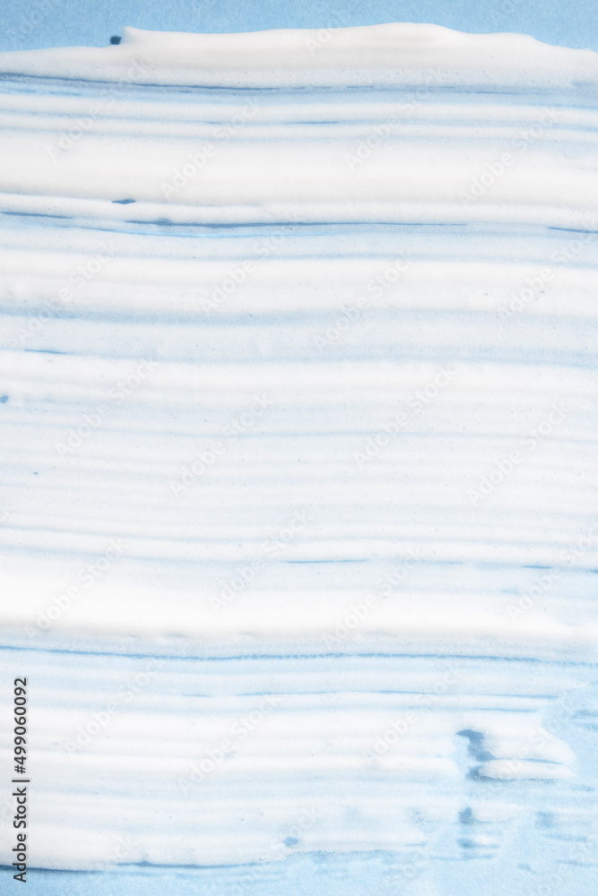 Texture of a white cosmetic product on a blue background, top view. Body cream, shampoo, lotion, foam for moisturizing and skin care, hygiene product close-up.