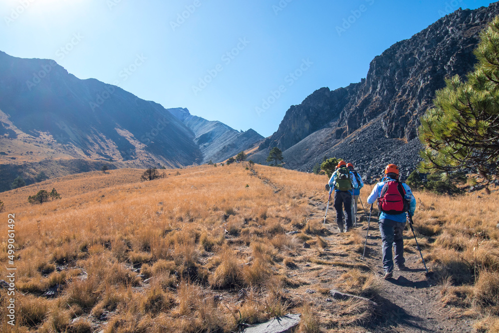 Group of hikers walking towards the mountain in the middle of a landscape with grass and rocky elevations on a sunny day in the Nevado de Toluca in Mexico