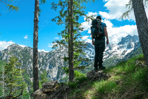 Man with backpack hiking on forest path with scenic view on sharp mountains Kamnik Savinja Alps in Carinthia, border Slovenia Austria. Velika Baba, Vellacher Kotschna. Mountaineering. Freedom concept