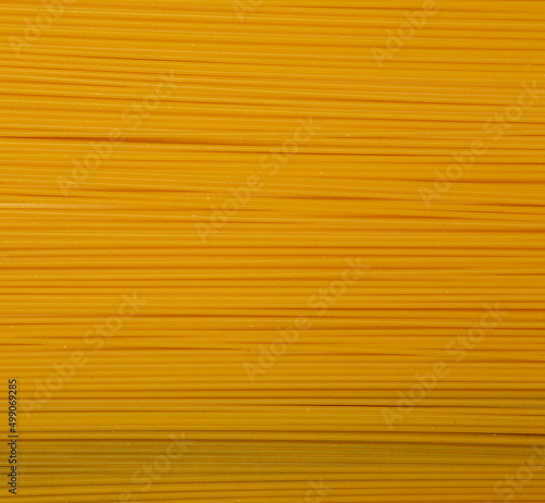 Yellow long spaghetti on a black background close-up. Thin pasta is arranged in rows. Yellow Italian pasta. Long spaghetti. Raw spaghetti wallpaper. Thin spaghetti. The concept of food products.