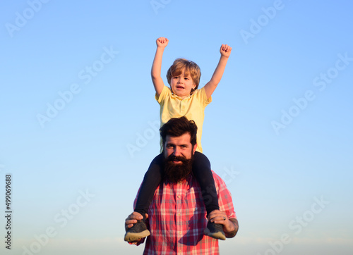 Son hugging his father against sky. Fathers day. Portrait of happy father giving son piggyback ride on his shoulders.