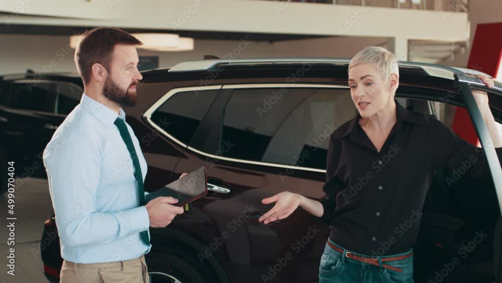 Salesman at the dealership showroom talking with customer and helping her to choosing a new car for herself in car showroom vehicle salon dealership store motor showroom. Buying car at dealership Salesman at the dealership showroom talking with customer and helping her to choosing a new car for herself in car showroom vehicle salon dealership store motor showroom. Buying car at dealership