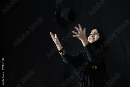muslim girl throwing graduation hat on black background
