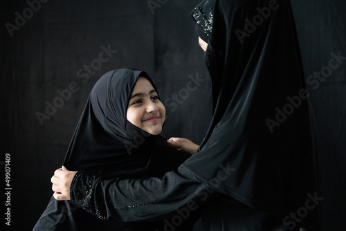 Bild auf Leinwand muslim woman and her daughter smiling and hugging together on black background