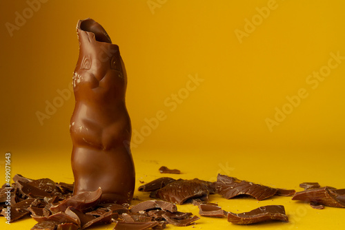 Chocolate Easter bunny with bitten ears and pieces scattered around. Copy space on yellow background. photo