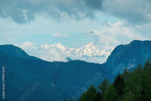 Scenic view on the snow capped and cloud covered mountains of Julian Alps and Kamnik Savinja Alps in Carinthia, border Austria and Slovenia. Dense green forest in spring in the valley. Mountaineering © Chris